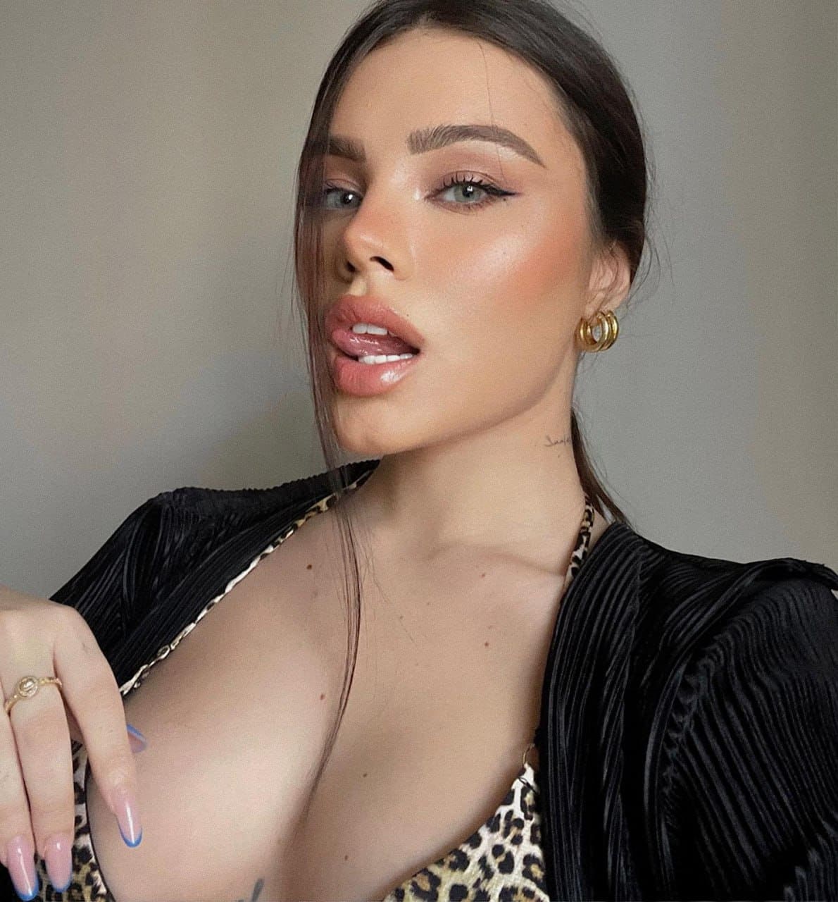 Close-up of a woman in a leopard-print top and open black pleated jacket, wearing gold earrings and a ring.