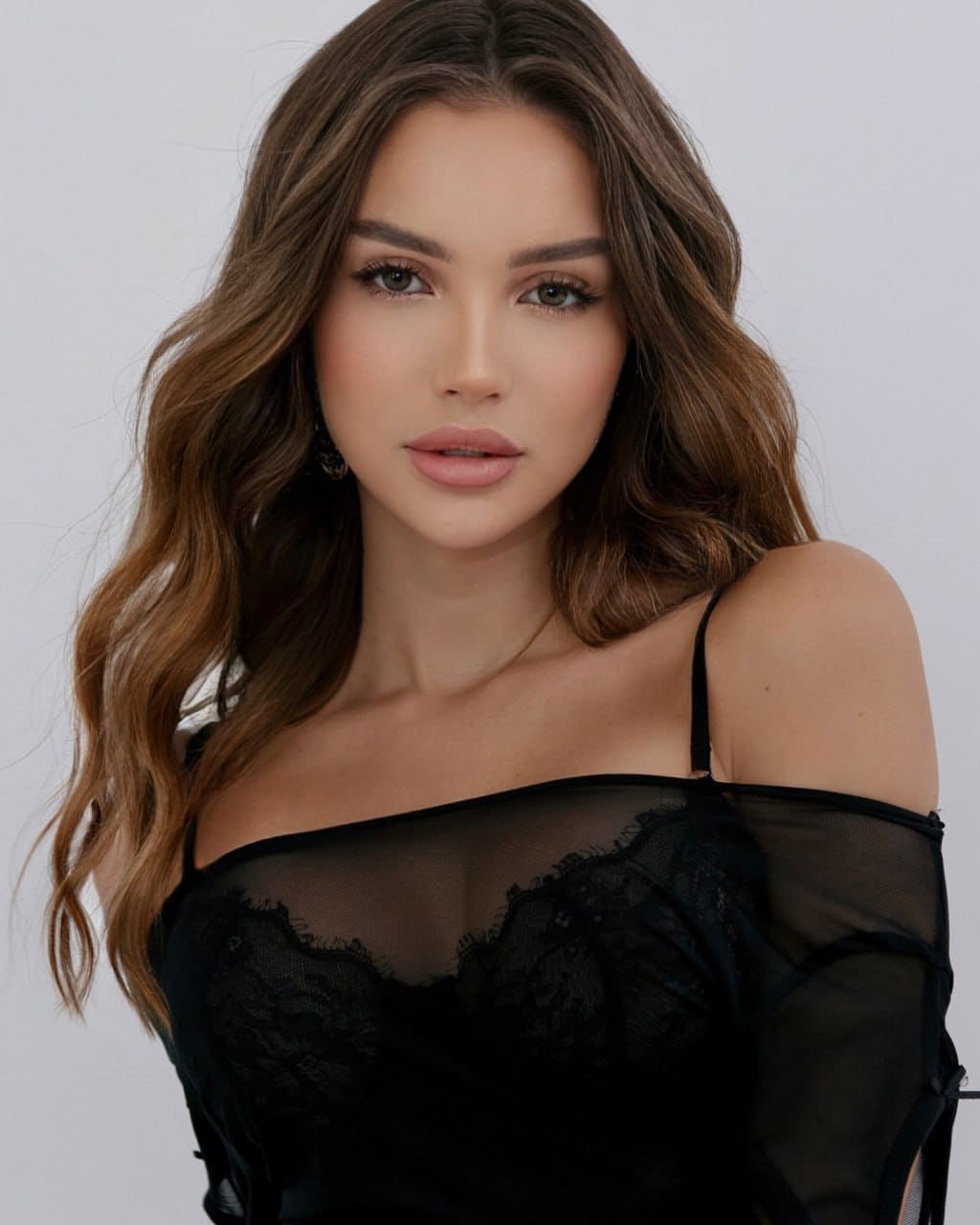 Margaret faces forward in a black off-shoulder top with sheer mesh sleeves and lace trim, against a plain light background.