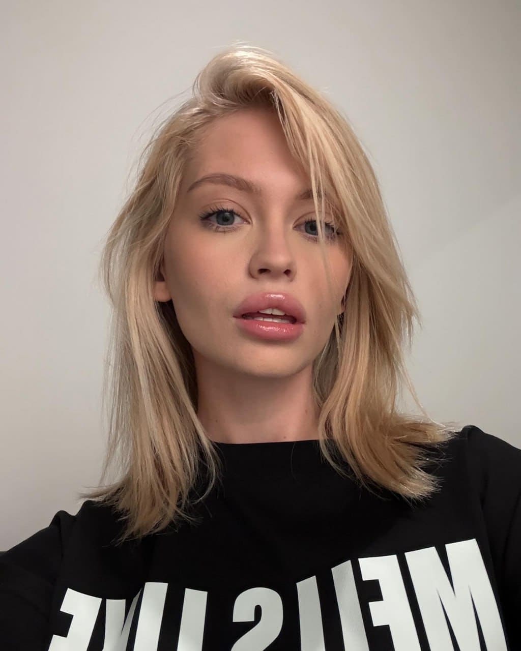 Chest-up portrait of a woman with shoulder-length blonde hair wearing a black sweatshirt with large white lettering.