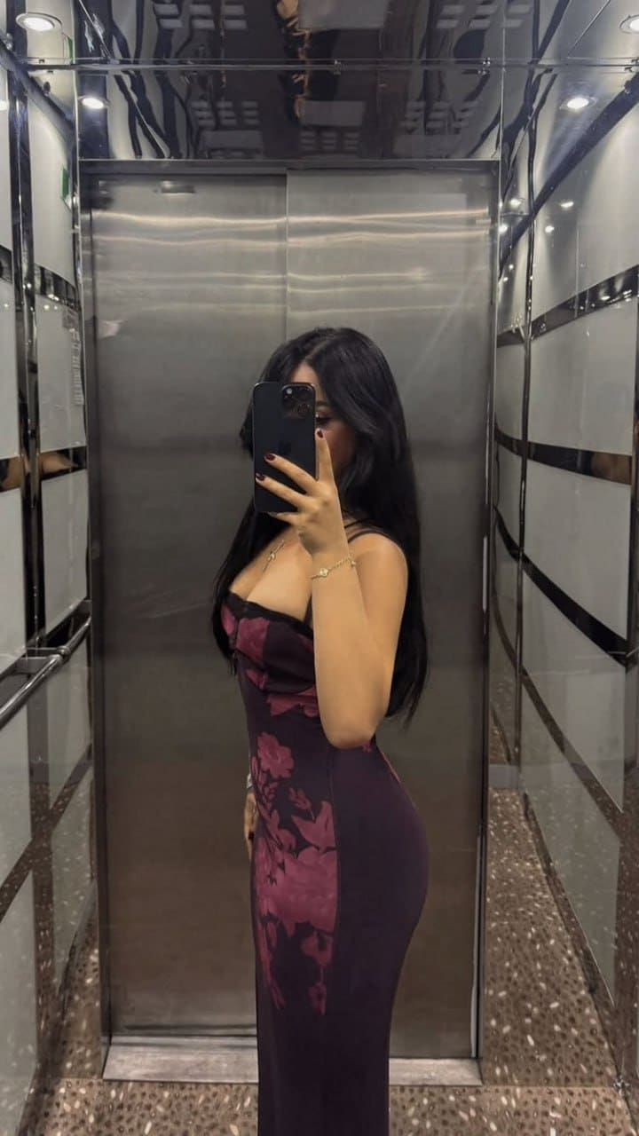 Mirror selfie in an elevator wearing a long dark floral dress with thin straps, a low neckline, and delicate jewelry.