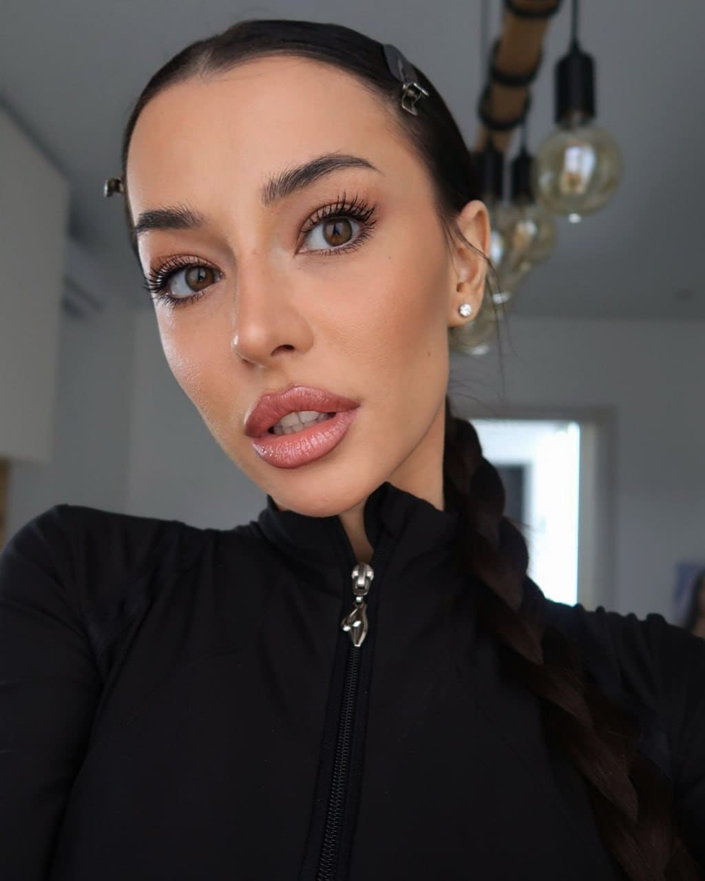 Indoor portrait features her in a black zip-up top with hair in a side braid, looking at the camera.
